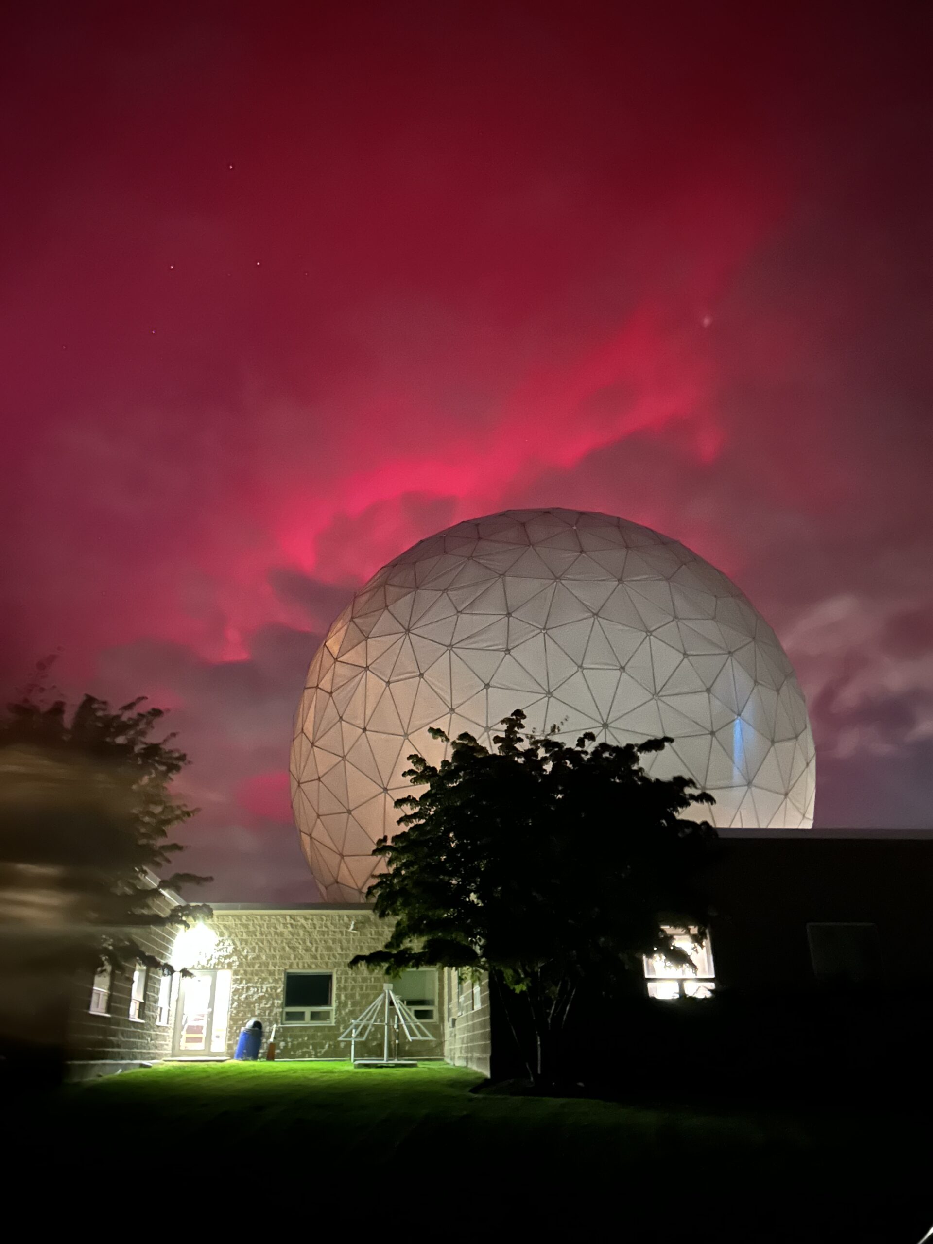 The white Haystack dome with vibrant pink aurora behind it