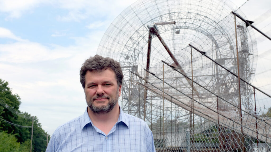 A man standing in front of a large radio radar antenna