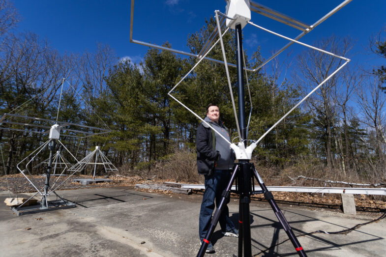 A man standing outside next to a tall antenna