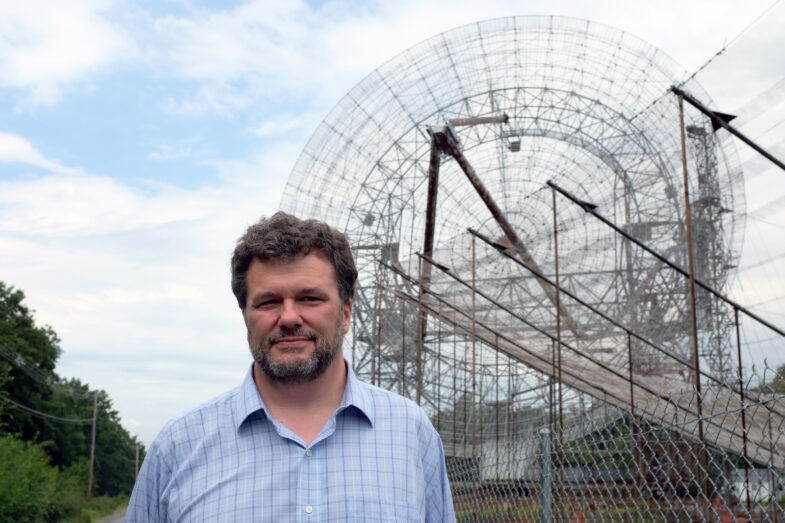 A man standing in front of a large radio antenna