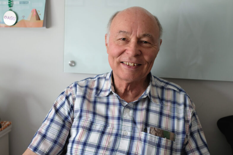 A man in a plaid shirt sitting and smiling at the camera