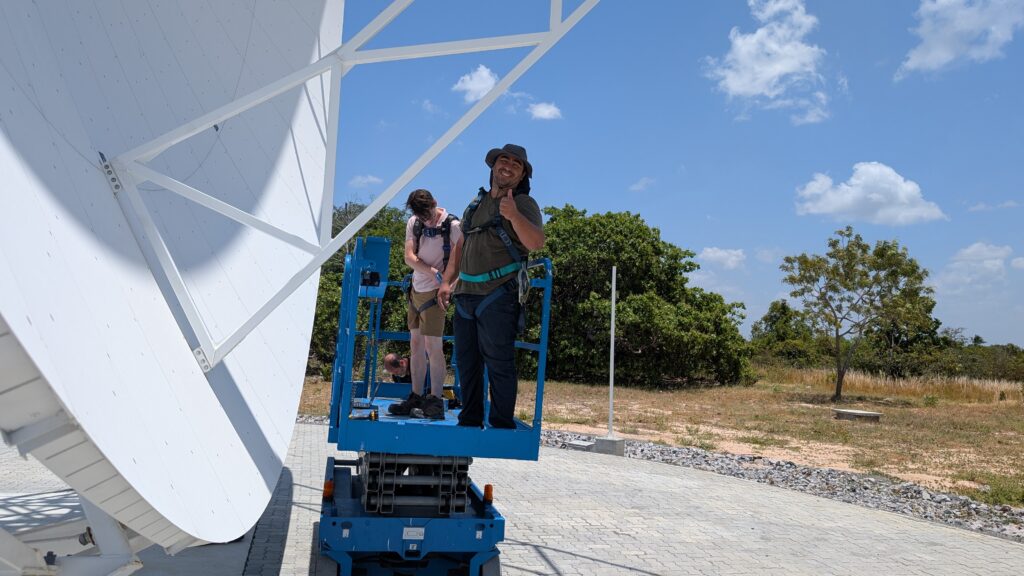 Two people on a lift next to a large white radio telescope dish