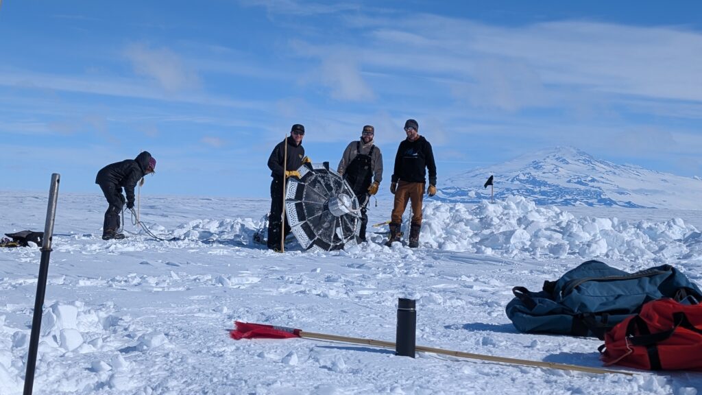 Four people on the snow and ice clearing off a large ice penetrator