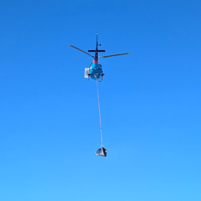 A helicopter carrying an item at the end of a long cable dangling underneath the helicopter